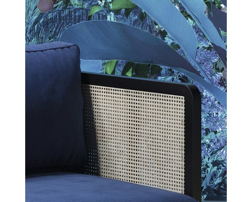 Detailopname van een blauwe fauteuil met rugleuning van rotan tegen een bloementapijt