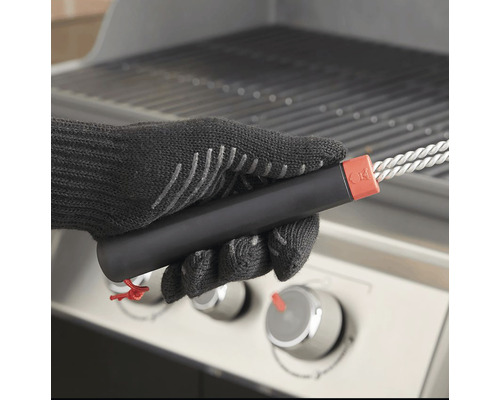 Een persoon met barbecuehandschoenen houdt een barbecueborstel voor een barbecue vast.