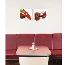 Twee muurafbeeldingen met chilipepermotieven boven een tafel