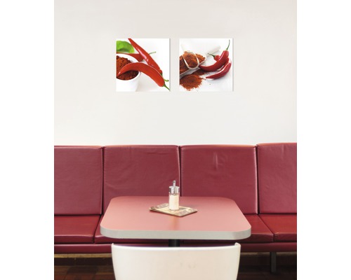 Twee muurafbeeldingen met chilipepermotieven boven een tafel
