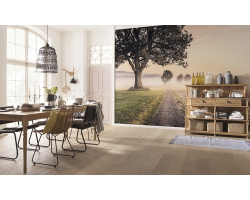 Eetkamer met houten tafel, stoelen, lamp en muurschildering met landschap.