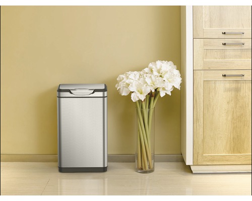 Roestvrijstalen afvalemmer naast een vaas met bloemen en een kast.