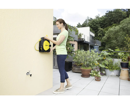 Vrouw monteert een slangentrommel aan een huismuur op een terras