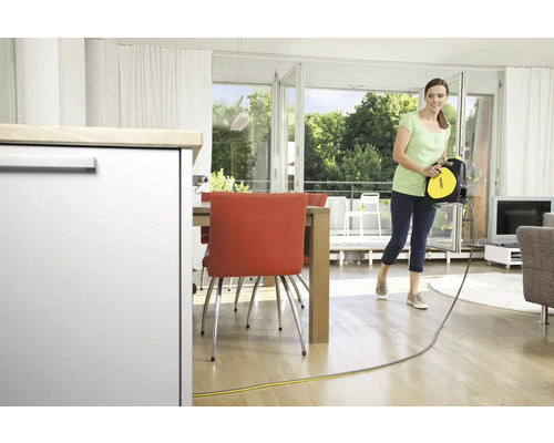 Vrouw draagt kabelhaspel van Kärcher in een woonkamer met eethoek.