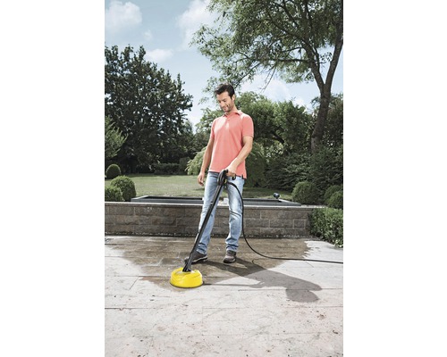 Een man reinigt een terras in de tuin met een terrasreiniger.