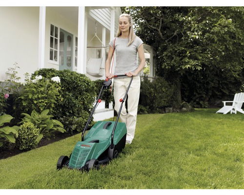 Vrouw bedient een gazonmaaier in de tuin.