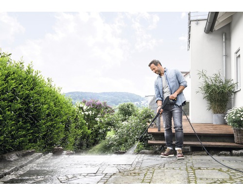 Een man reinigt met een hogedrukreiniger een stenen terras voor een huis.