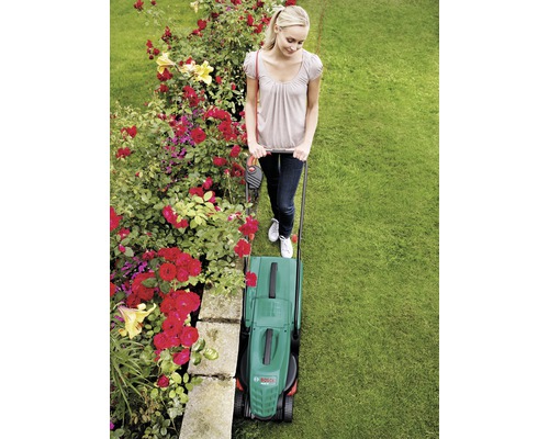 Vrouw maait gazon met een elektrische grasmaaier in de tuin.