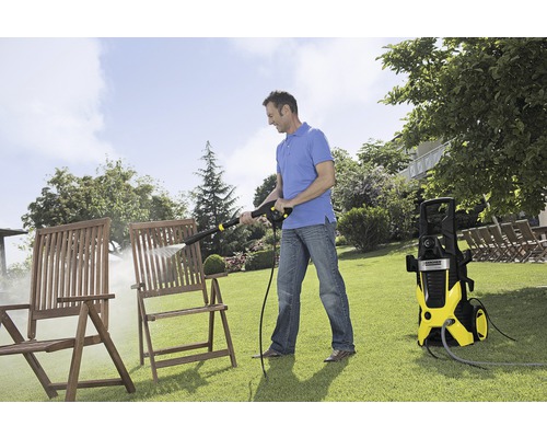 Een man reinigt houten stoelen met een hogedrukreiniger in de tuin.
