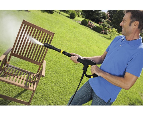 Een man reinigt een houten stoel met een hogedrukreiniger in de tuin.