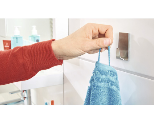 Een hand hangt een blauwe handdoek aan een handdoekhaak in de badkamer