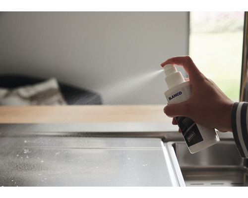 Een hand spuit reiniger uit een Blanco spuitfles op een roestvrijstalen spoelbak.