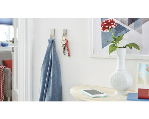 Scene met twee zelfklevende haken waar een shirt en een sleutelbos aan hangen, plus een tafel met een bloemenvaas en smartphone