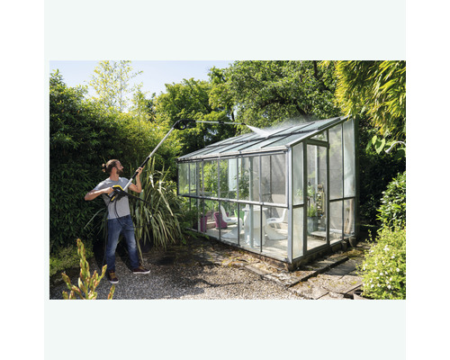 Man reinigt een glazen kas met een hogedrukreiniger in de tuin.