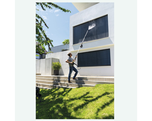 Een man maakt met een hogedrukreiniger de ramen van een huis schoon.