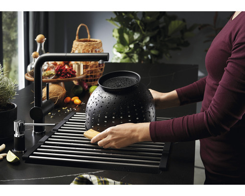 Keukenscène met gootsteen, afdruiprek, kraan en een persoon die een vergiet afwast