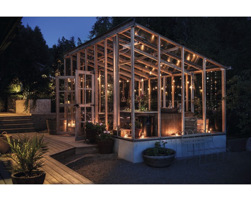 Kas met houten frame, glazen wanden en verlichting in de tuin ''s nachts.