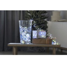 Decoratieve scène met glazen vaas, lichtsnoer en cadeaus op een tafel voor een kerstboom