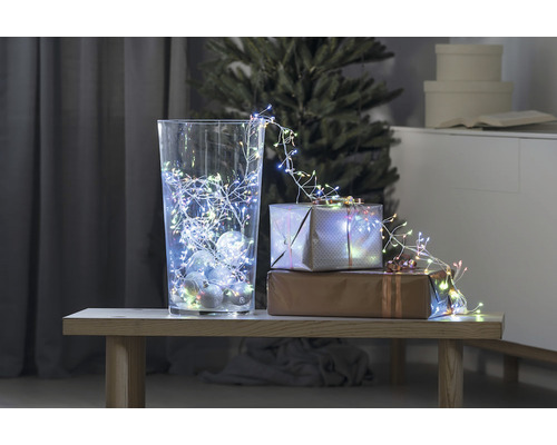 Decoratieve scène met glazen vaas, lichtsnoer en cadeaus op een tafel voor een kerstboom