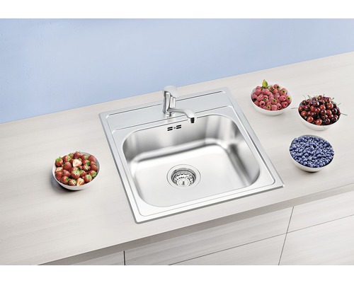 Roestvrijstalen spoelbak met kraan en kommen met fruit op een aanrecht