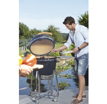 Keramische barbecue op wielen met open deksel en iemand die aan het grillen is