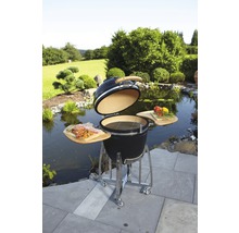 Keramische barbecue met open deksel, houten planken en roestvrijstalen frame in een tuinscène