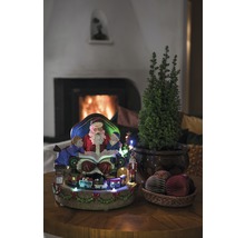 Kerstdecoratie met kerstman, kinderen, trein, klein boompje en decoratieve ballen op een tafel voor een open haard.