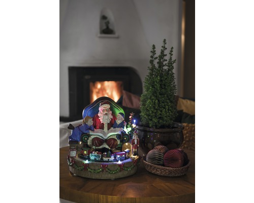 Kerstdecoratie met kerstman, kinderen, trein, klein boompje en decoratieve ballen op een tafel voor een open haard.
