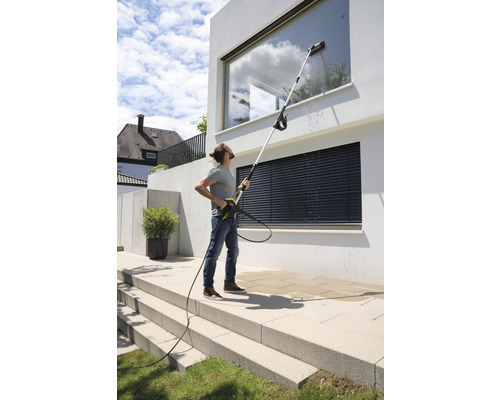 Een persoon reinigt ramen van een modern huis met een hogedrukreiniger en een telescopische lans.
