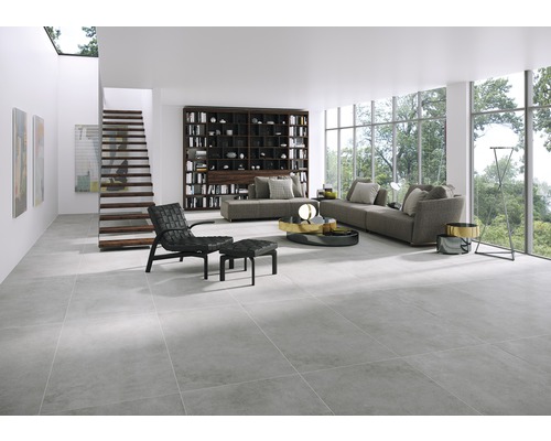 Lichte woonkamer met grijze vloertegels, bank, boekenkast en trap