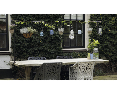 Tuinscene met houten tafel, stoelen en decoratieve hangende elementen aan een met klimop begroeide muur