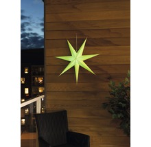 Decoratieve papieren ster aan een houten wand, met een stoel en een plant in beeld.