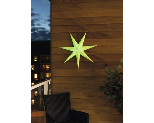 Decoratieve papieren ster aan een houten wand, met een stoel en een plant in beeld.