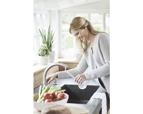 Vrouw bij de gootsteen in een lichte keuken met kraan en verse groenten