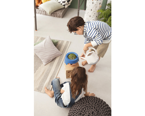 Twee kinderen binnen, waarvan één een plant in een bloempot met gezicht water geeft met een gieter.