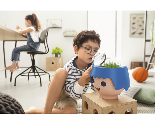 Jongen bekijkt plant in een plantenbak met een vergrootglas in een kinderkamer.