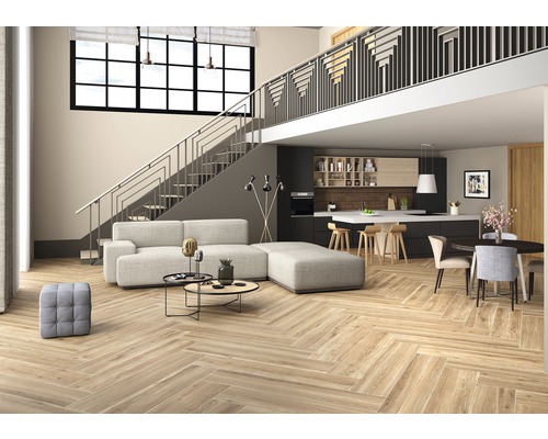 Lichte woonkamer met visgraat parketvloer, trap en open keuken.