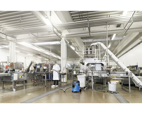 Een persoon gebruikt een nat- en droogzuiger in een industriële hal.