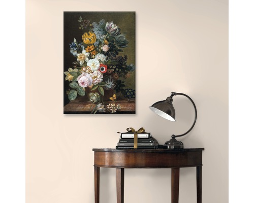 Schilderij met bloemstilleven boven boeken en een lamp op een tafel