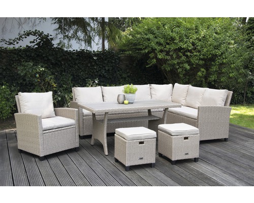 Tuinmeubelset met tafel, hoekbank, fauteuil en krukjes op een terras voor een groene haag.