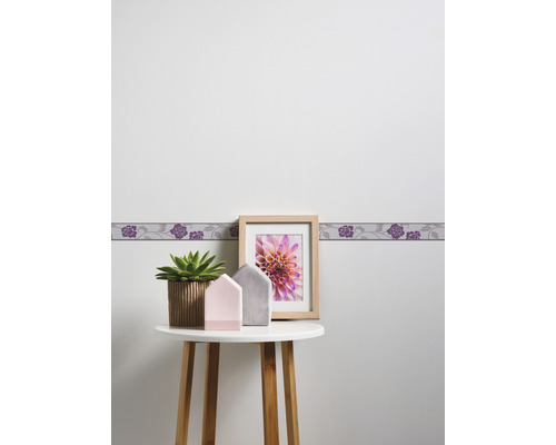 Scene met behangrand, fotolijst, plant en decoratie op een tafel.