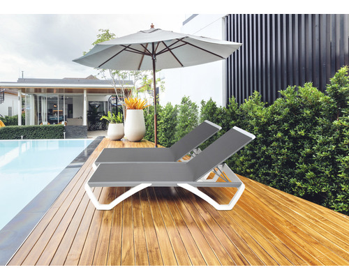 Twee grijze kunststof ligstoelen met een parasol naast een zwembad.