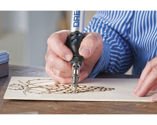 Iemand gebruikt een Dremel brandpunt om een druivenmotief in een stuk hout te branden.
