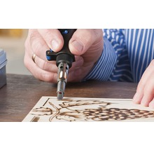 Man brandt met een soldeerbout een druivenmotief in een houten plank.