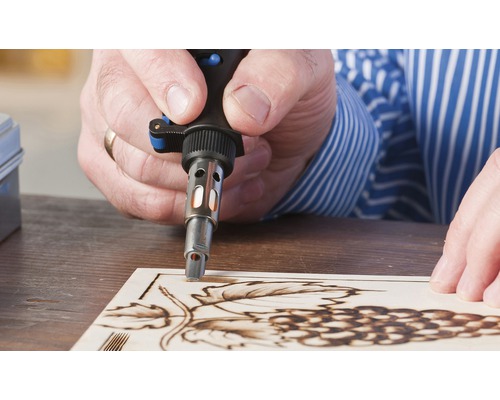 Man brandt met een soldeerbout een druivenmotief in een houten plank.