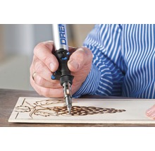 Een persoon gebruikt een Dremel brandgereedschap om een druivenmotief in een houten plank te branden.