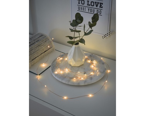KONSTSMIDE Kerstverlichting LED lichtsnoer 20 lampjes extra warmwit met 6 uur timer 1,9 m Decoratieve lichtslinger op een tafel met vaas en plant.