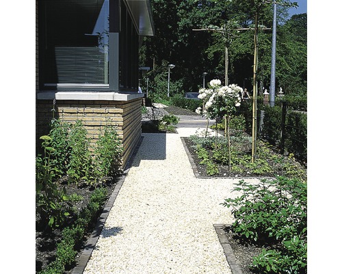 Tuinpad met grind naast een woonhuis met beplanting.