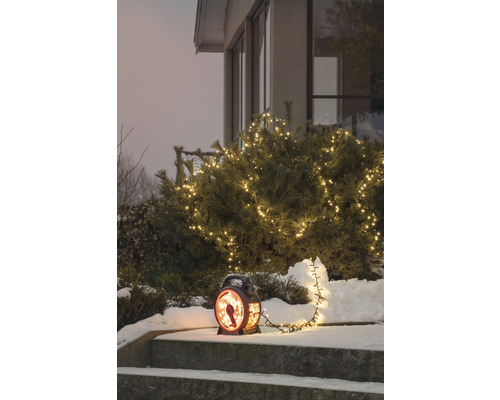 Winterse tuinscène met verlichte struik en decoratieve lantaarn op een trap