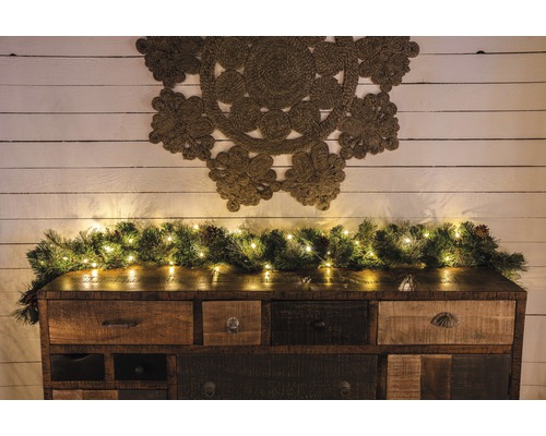 KONSTSMIDE Kerstverlichting LED druppellichtsnoer 50 lampjes extra warmwit 4,9 m Decoratief dressoir met dennen slinger en lichtsnoer, en een wandkleed aan de muur.